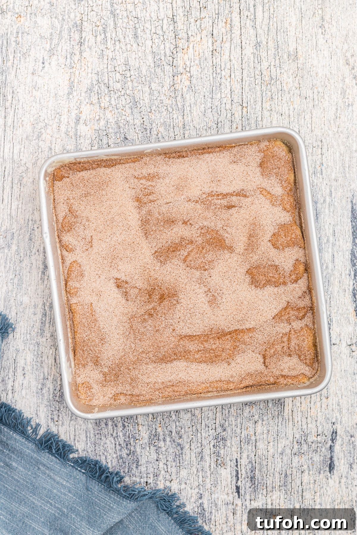Churro Cheesecake Recipe: Cinnamon-Sugar Cheesecake Bars 9 Top of square cheesecake topped with melted butter and sugar and cinnamon mixture, before baking.