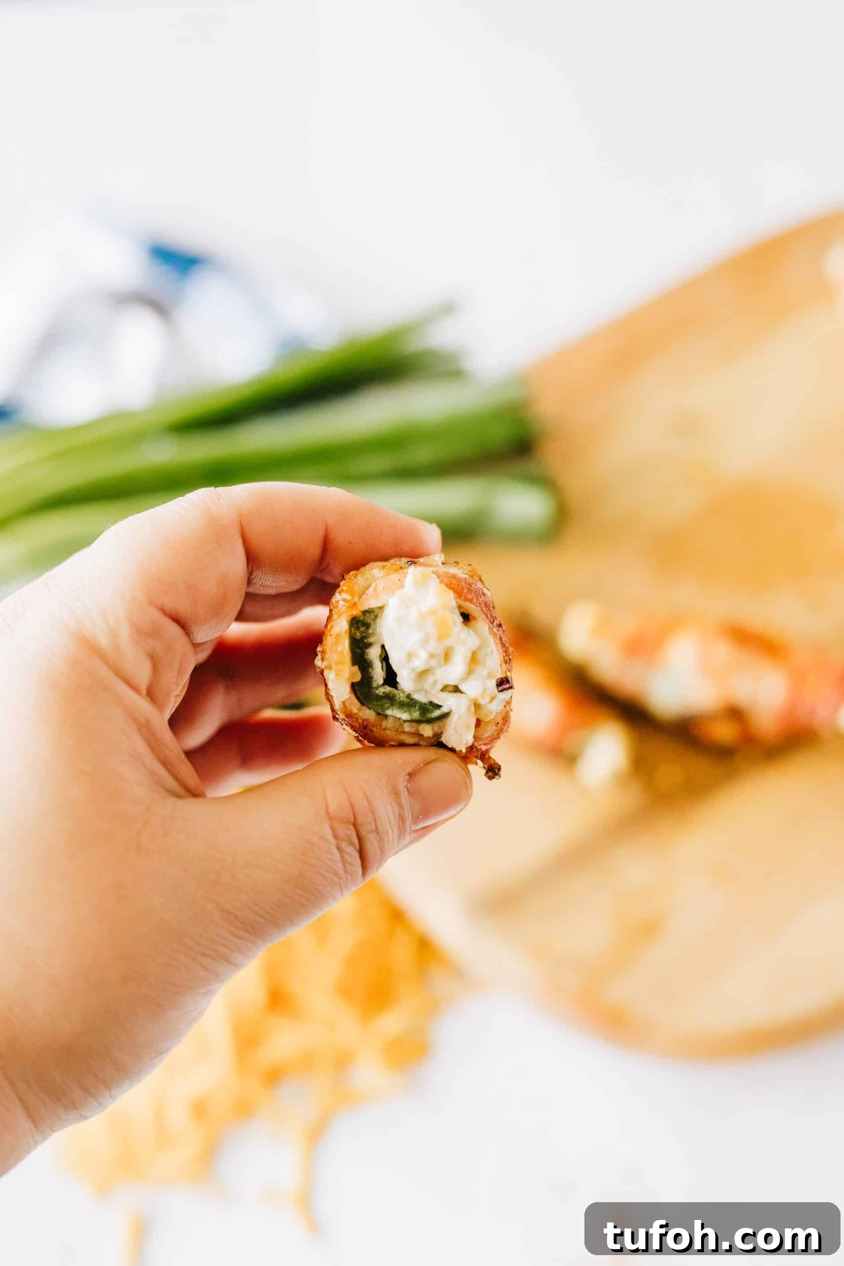 a hand holding up a half of a grilled jalapeno popper showing the creamy filling inside