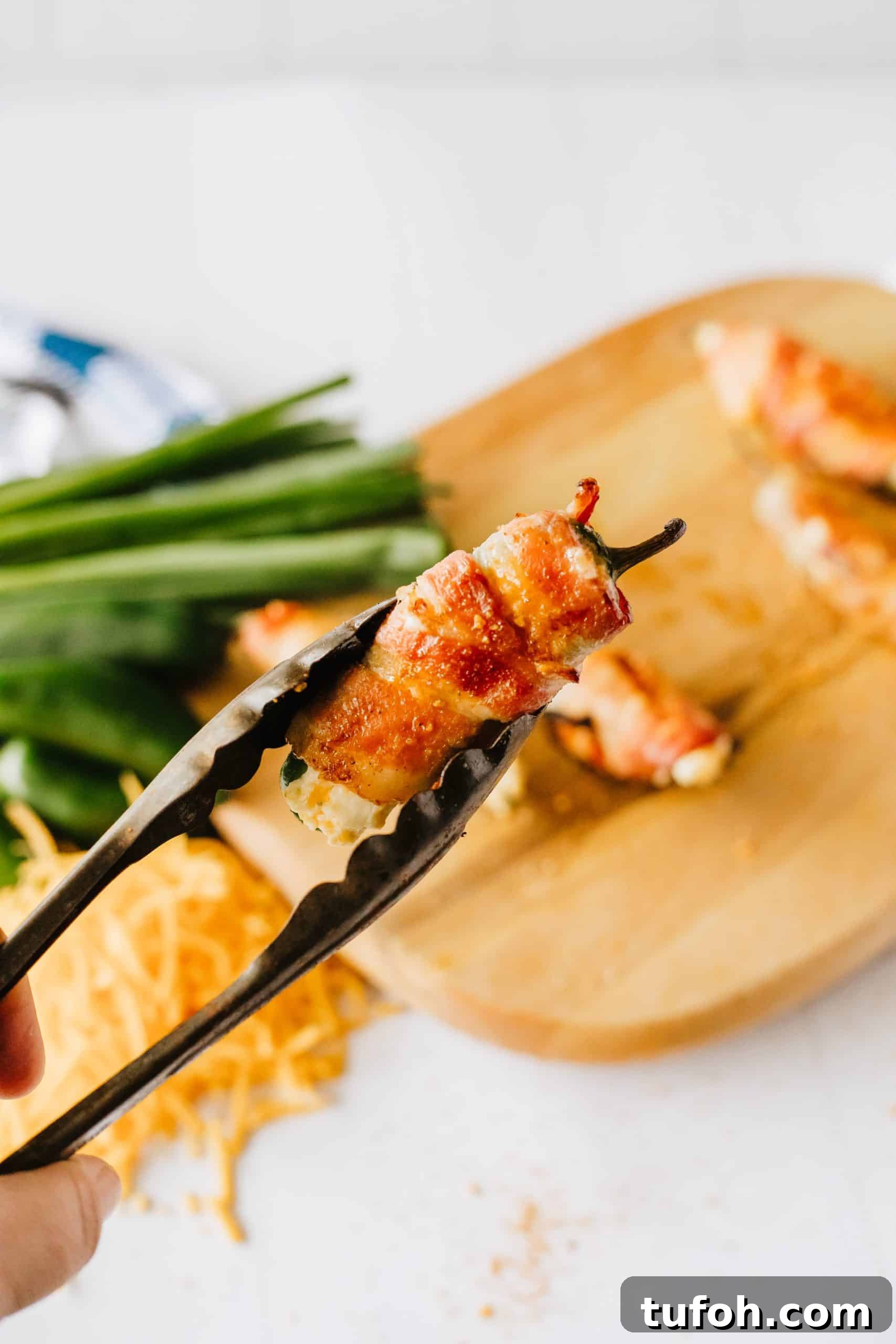 metal tongs holding up a bacon wrapped grilled jalapeno popper