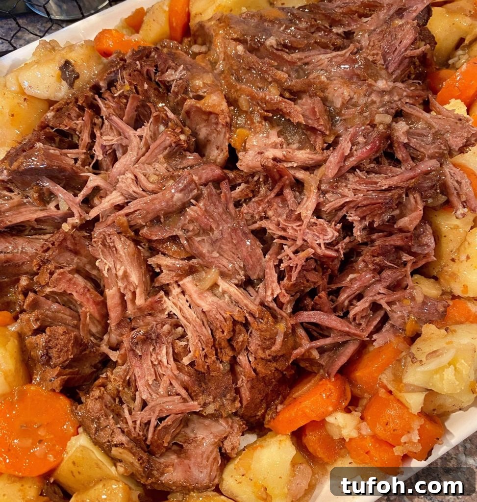 Best Pot Roast shredded on a serving platter with potatoes and carrots surrounding it.