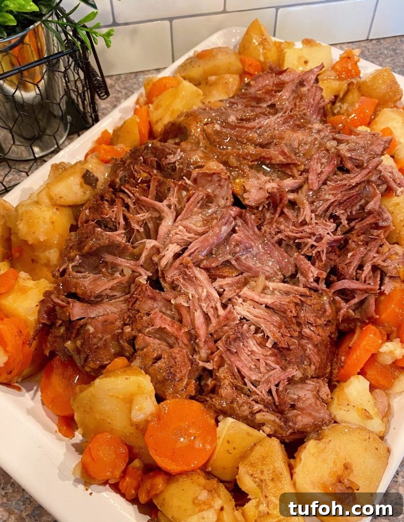 Best Pot Roast on a platter shredded with potatoes and carrots surrounding it.