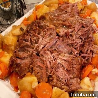 Best Pot Roast on a platter shredded with potatoes and carrots surrounding it.