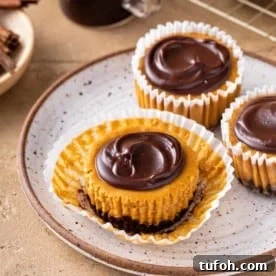 Unwrapped mini pumpkin cheesecake set on a plate next to two other mini pumpkin cheesecakes.