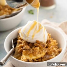 Caramel sauce being drizzled over apple pear crisp and whipped cream in a white bowl