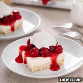 Slice of nana's easy cheesecake, topped with cherry pie filling and whipped cream, on a white plate.