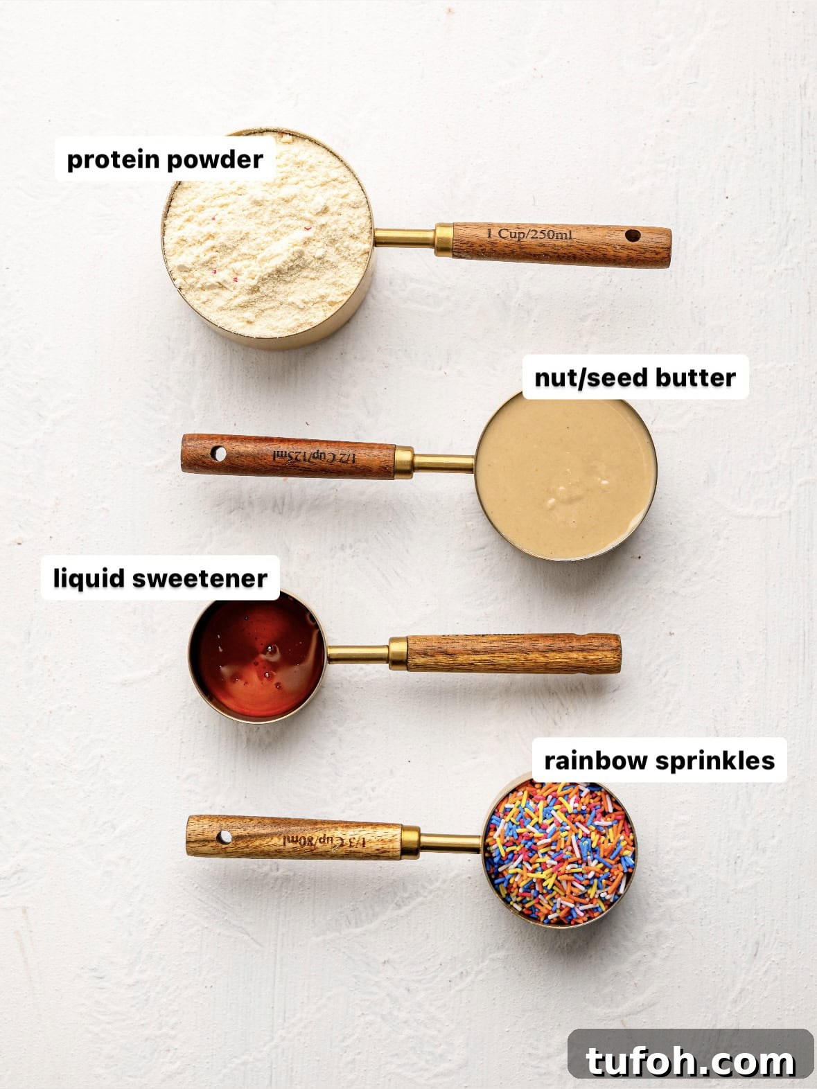 Birthday cake protein bar ingredients in measuring cups: protein powder, nut/seed butter, liqudi sweetener and sprinkles.