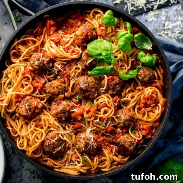 Spaghetti and meatballs in a black pan topped with grated cheese and basil.