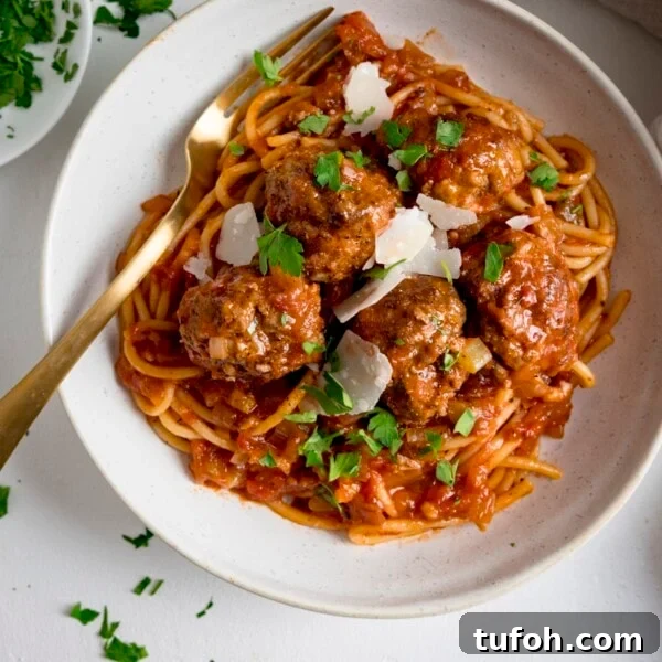 Spaghetti and meatballs in tomato sauce in a white bowl with a gold fork.