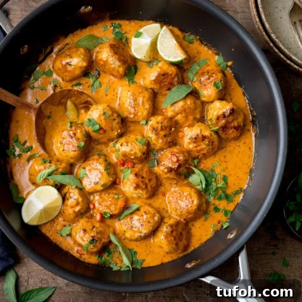 Thai Chicken Meatball Curry in a black pan with a wooden spoon, lime wedges and herbs.