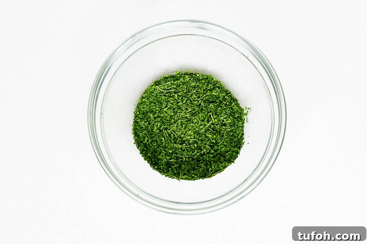 Oven-Dried Parsley: A Simple Guide for Long-Lasting Flavor 9 Crumbled oven dried parsley with larger stems removed, in a glass bowl viewed from above.