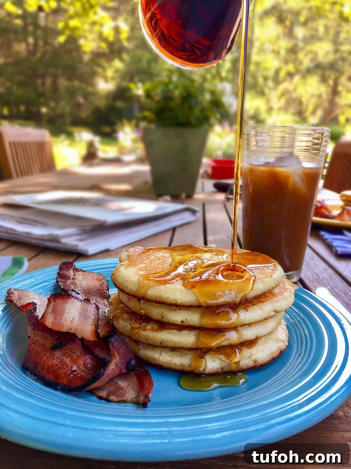 A blue plate topped with three light and fluffy pancakes, maple syrup, and cooked bacon.
