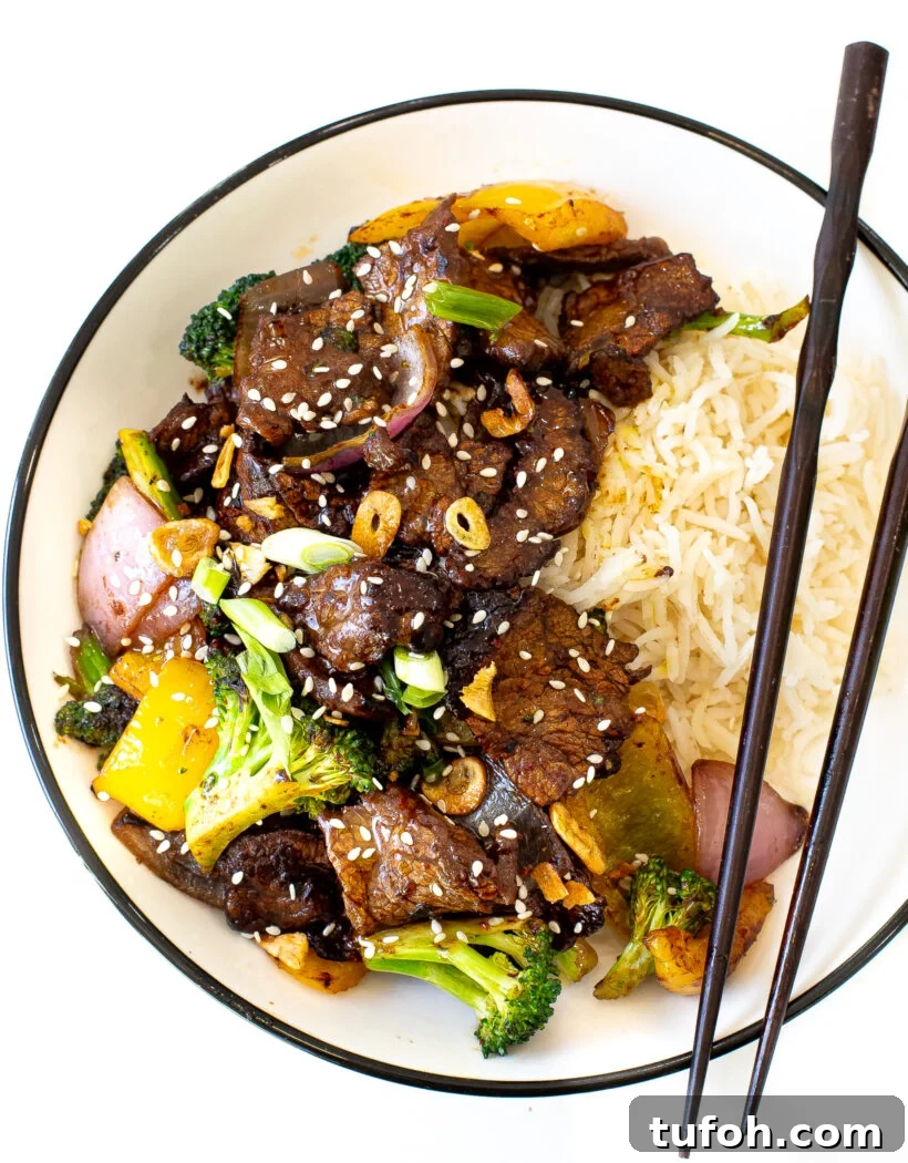 Beef Stir Fry and rice in a white bowl with black chopsticks laying across the bowl.