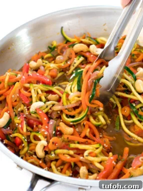 this zucchini noodle stir fry with cashews in a metal skillet with metal tongs tossing the noodles in the sauce | chefsavvy.com