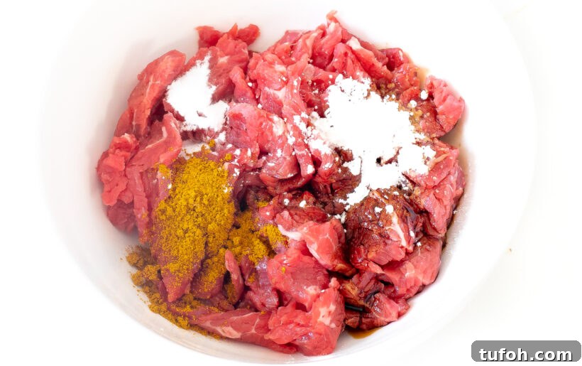Sliced flank steak in a bowl with marinade ingredients.