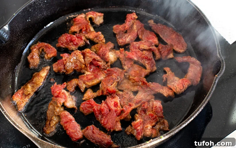 Sliced flank steak in a skillet with oil.