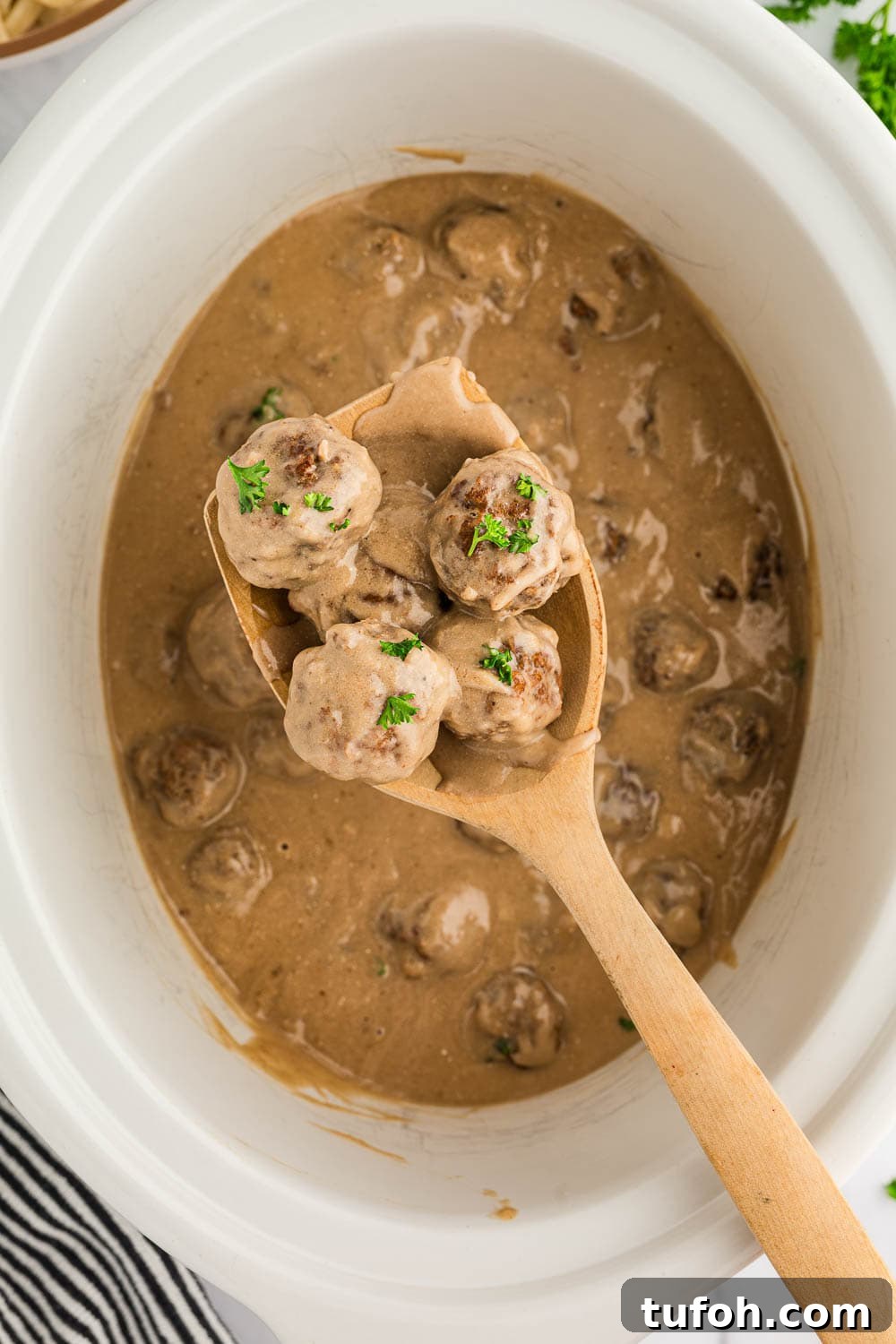 Swedish Meatballs in Slow Cooker with Creamy Sauce 5 Slow Cooker Swedish Meatballs cooked in slow cooker with wooden spoon picking up 4 meatballs