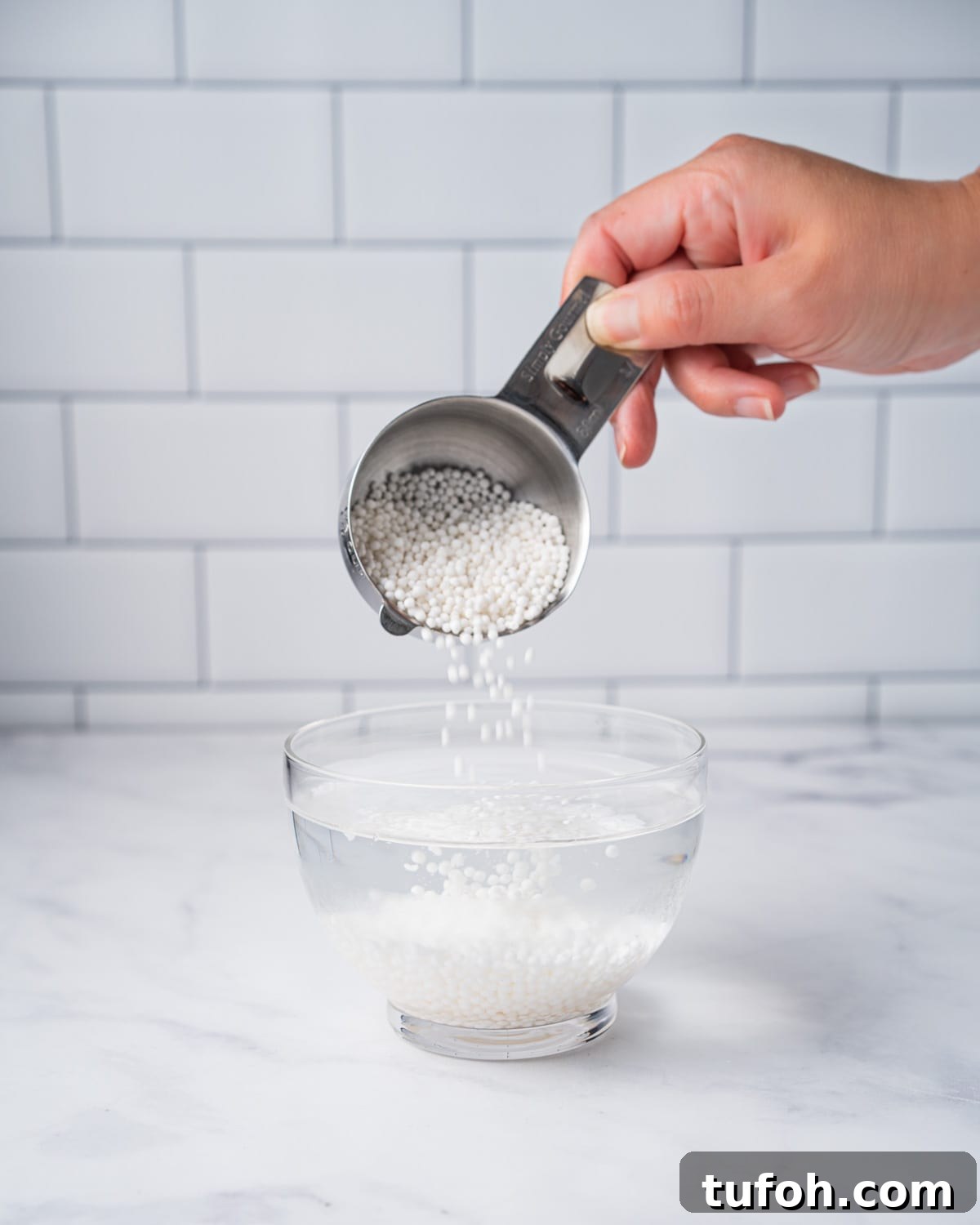 Adding tapioca pearls into a clear glass bowl of water.
