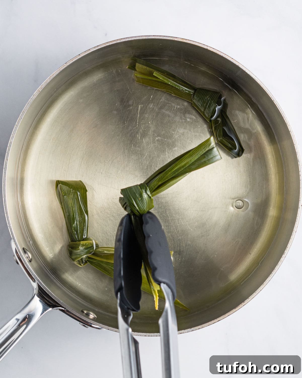 Tongs taking out pandan leaves tied in a knot.