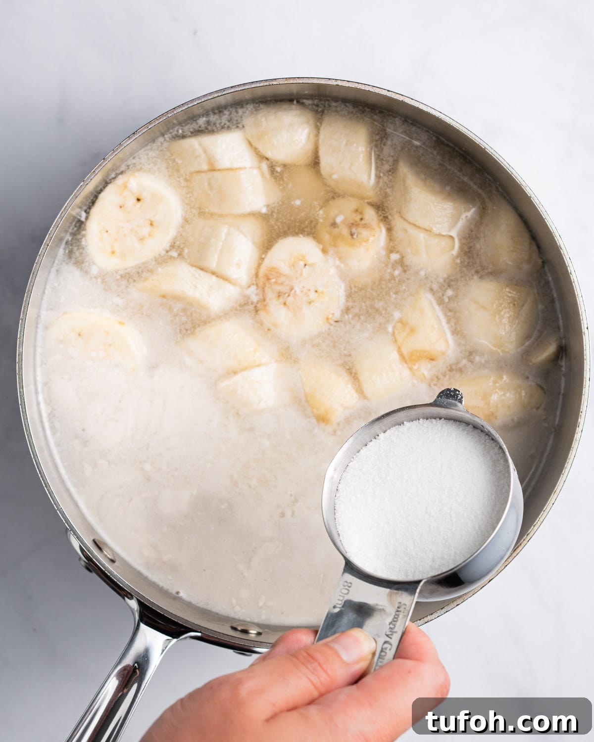 Adding sugar into pot with pandan infused coconut milk, banana, and tapioca pearls.