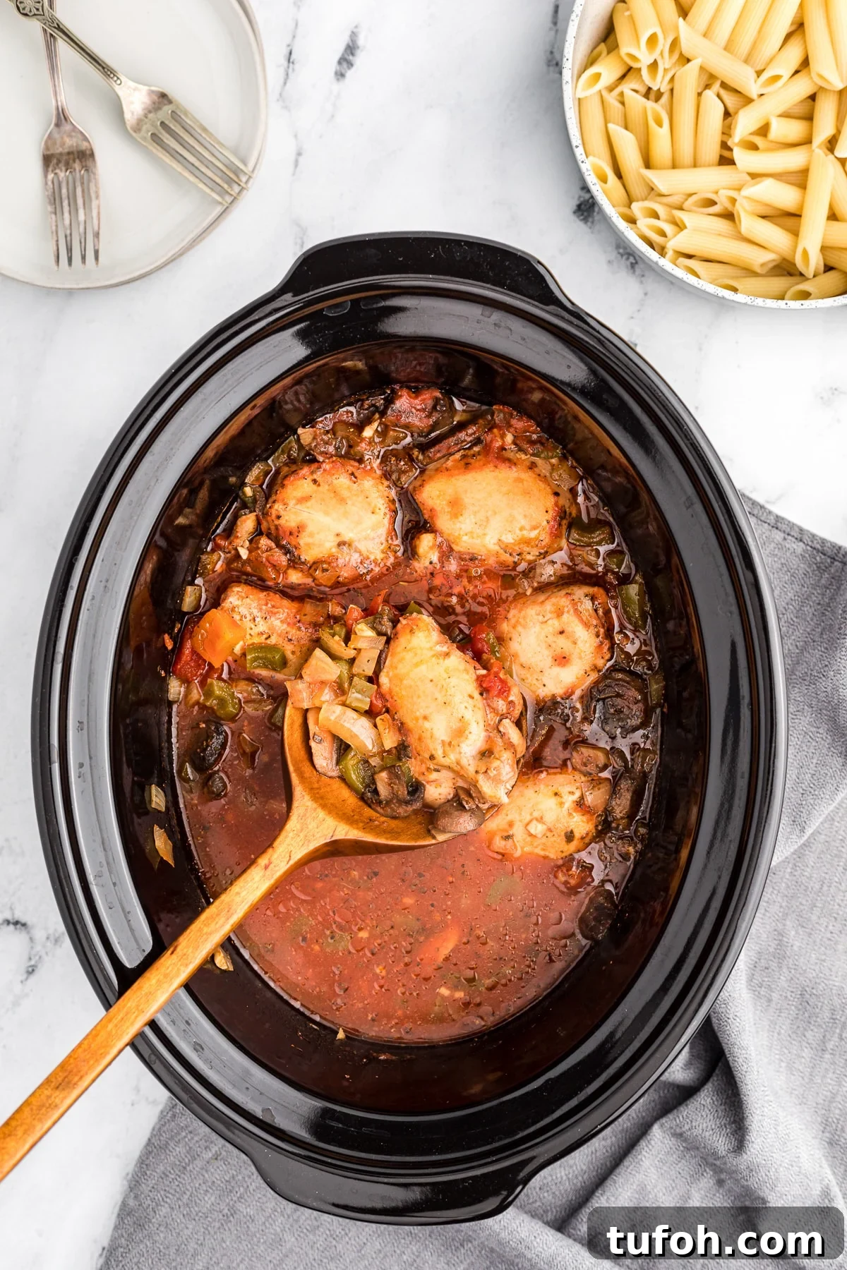 chicken cacciatore cooked in slow cooker with wooden spoon.
