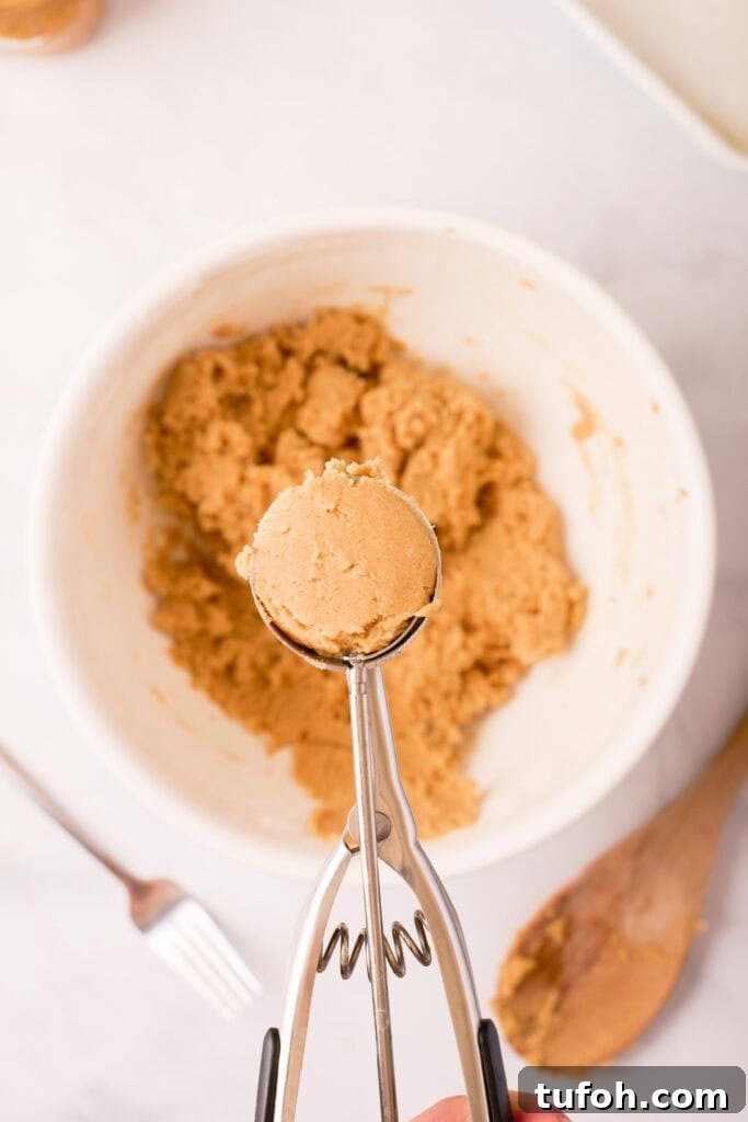 Chewy Peanut Butter Cookies Recipe with Crispy Edges 12 Cookie scoop holding a portion of peanut butter dough above the mixing bowl, showing the dough’s soft texture before baking.