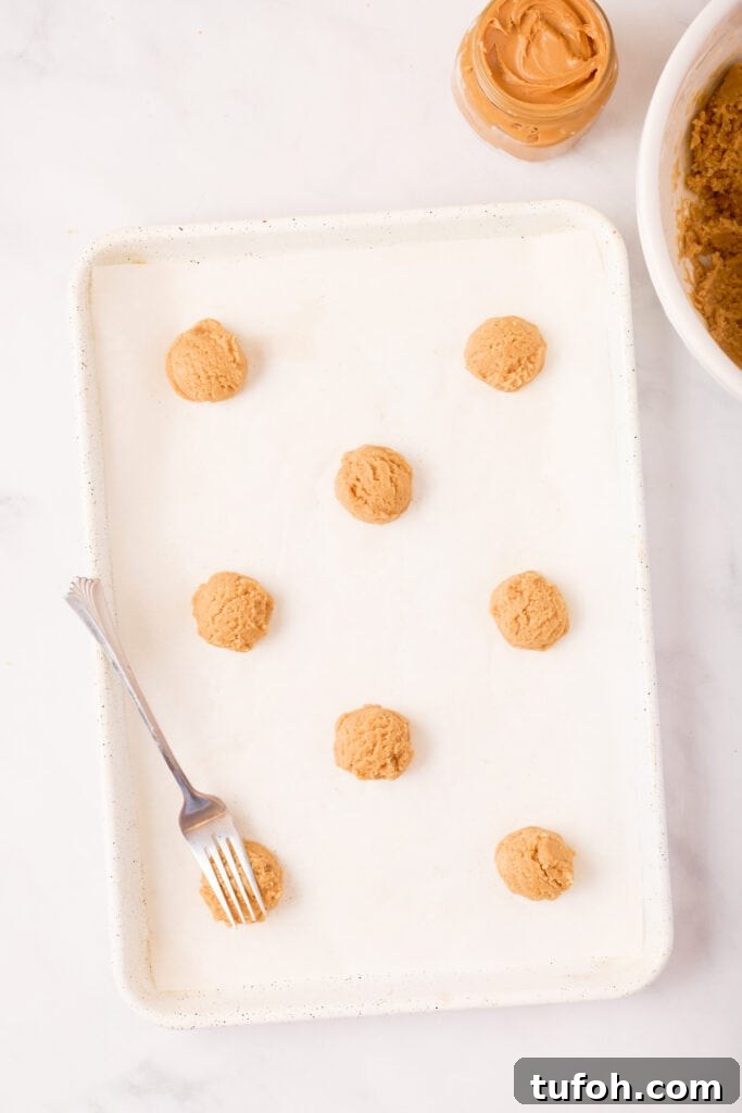 Chewy Peanut Butter Cookies Recipe with Crispy Edges 13 Baking sheet lined with parchment paper showing scoops of peanut butter cookie dough spaced apart with a fork ready for crisscrossing.