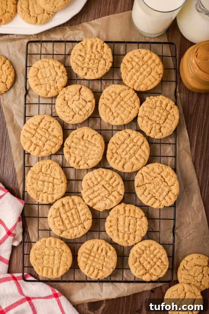 Chewy Peanut Butter Cookies Recipe with Crispy Edges 16 Peanut butter cookies cooling on a wire rack with parchment underneath, surrounded by milk and a jar of peanut butter.