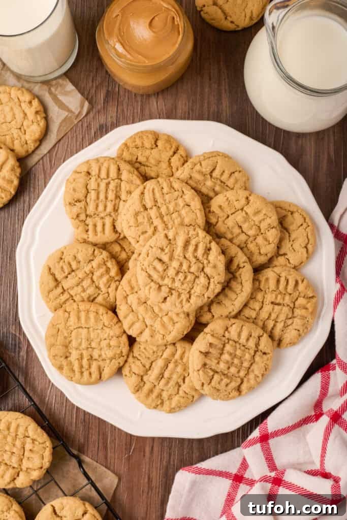 Chewy Peanut Butter Cookies Recipe with Crispy Edges 17 Plate piled high with peanut butter cookies beside a jar of peanut butter and glasses of milk on a wooden table.