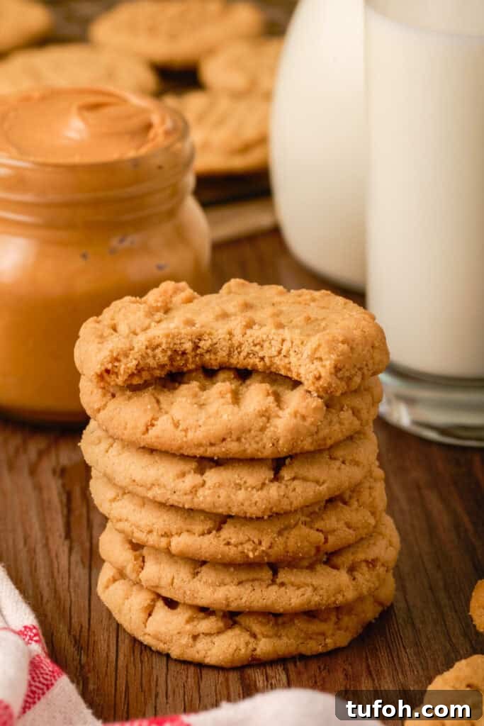 Chewy Peanut Butter Cookies Recipe with Crispy Edges 18 Stack of peanut butter cookies with a bite taken from the top cookie, sitting beside milk and peanut butter.