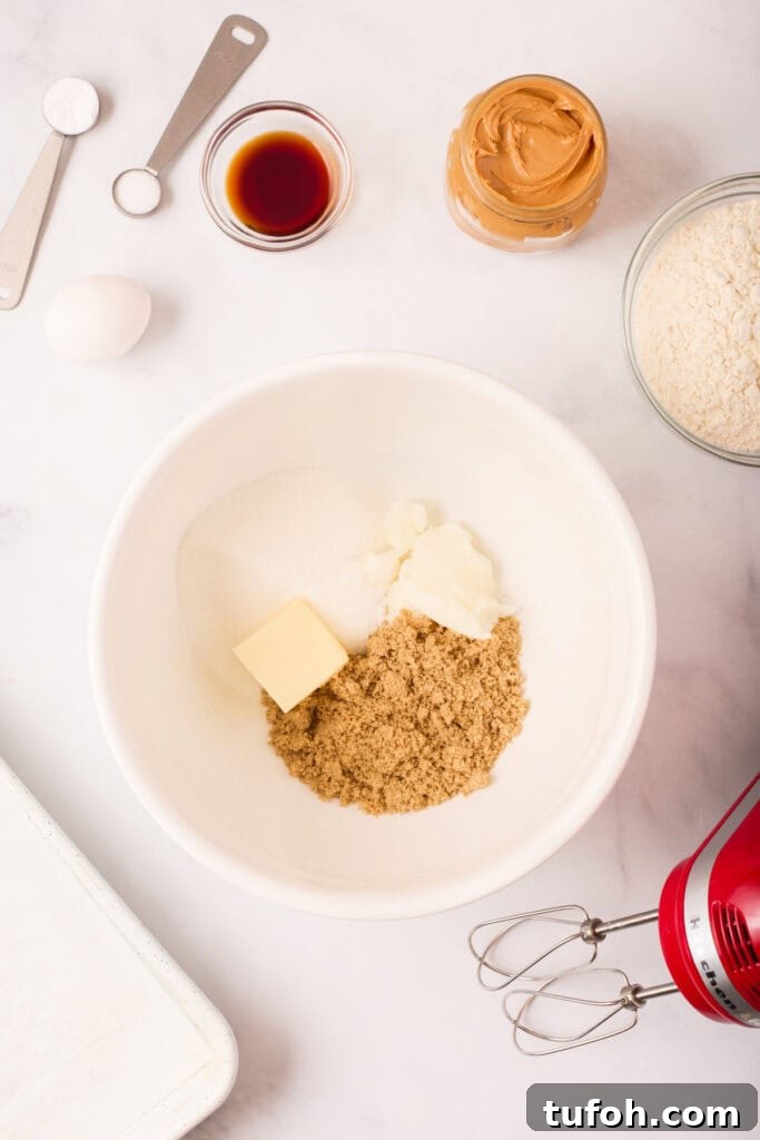 Chewy Peanut Butter Cookies Recipe with Crispy Edges 4 Mixing bowl with butter, shortening, brown sugar, and granulated sugar before creaming, surrounded by additional cookie ingredients and a red hand mixer.