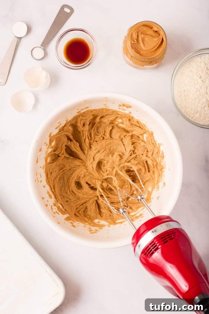 Chewy Peanut Butter Cookies Recipe with Crispy Edges 9 Fully combined peanut butter cookie batter, light brown and creamy in texture, shown in a mixing bowl with the hand mixer resting beside it.