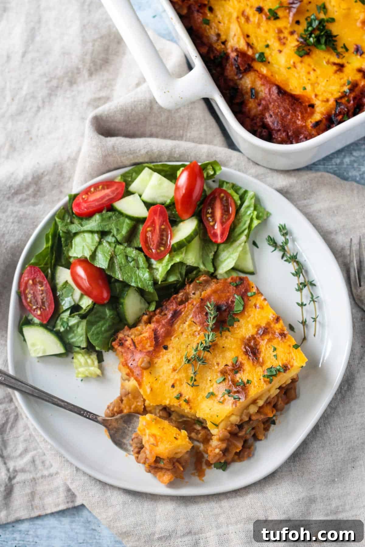 Slice of lentil shepherd's pie on a plate with a side of salad.