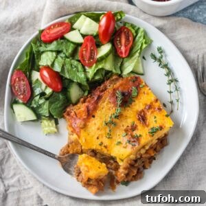 Slice of lentil shepherd's pie on a plate with a side of salad.
