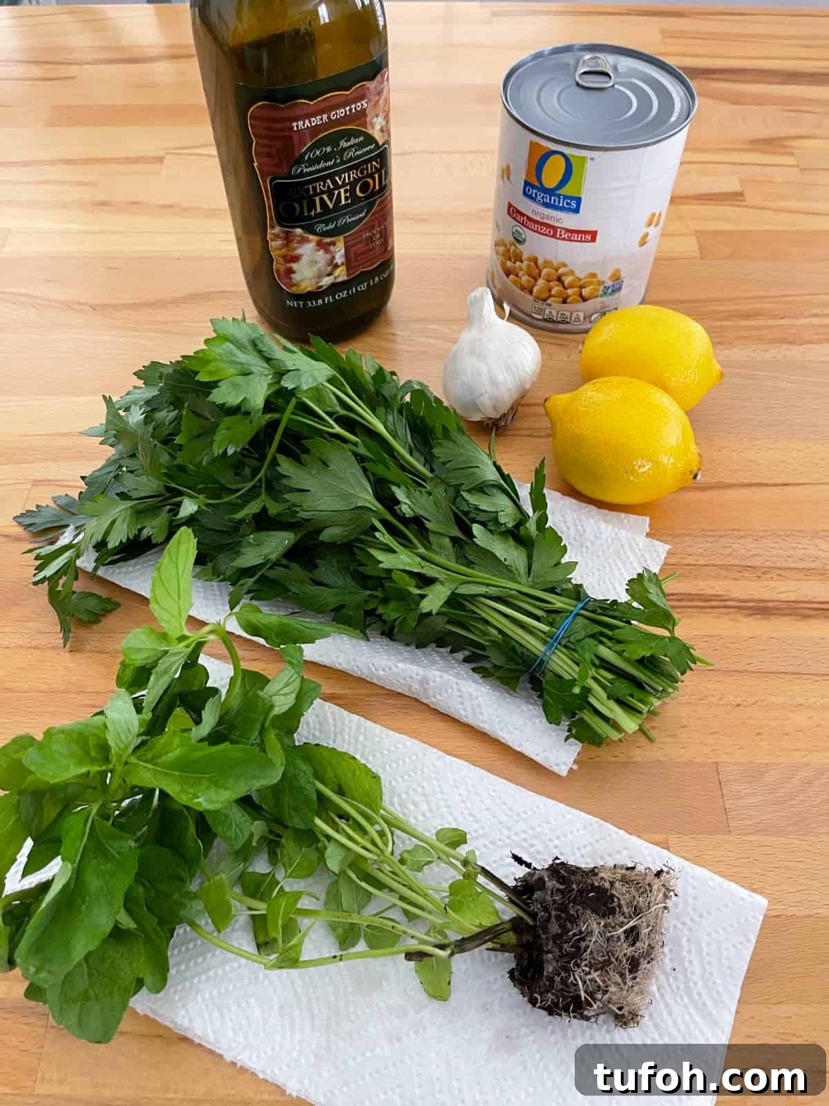 Gluten-Free Low-Carb Chickpea Tabbouleh Recipe 3 Ingredients including olive oil, canned garbanzo beans, lemons, garlic, parsley and mint on wood table.