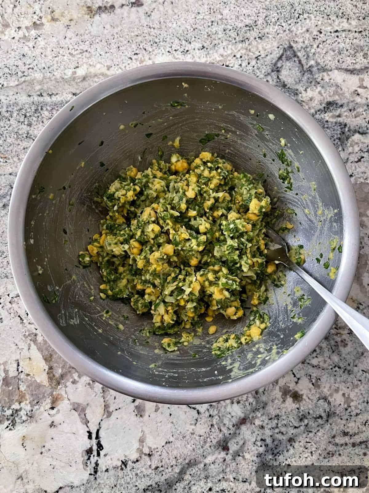Gluten-Free Low-Carb Chickpea Tabbouleh Recipe 5 Mixing chickepea tabbouleh with fork in stainless bowl on granite counter.