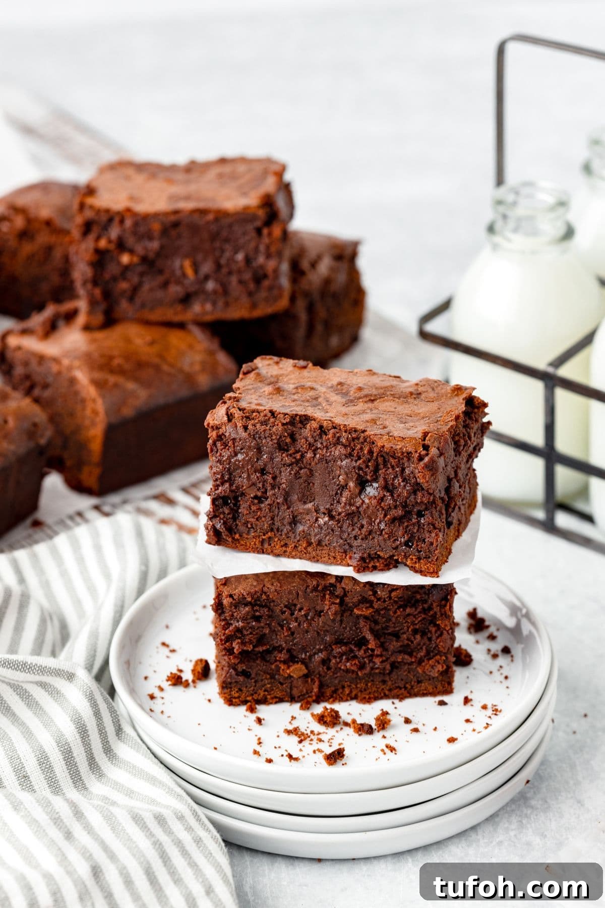 Two stacked chocolate brownies sit on a small pile of white plates, with crumbs scattered around.