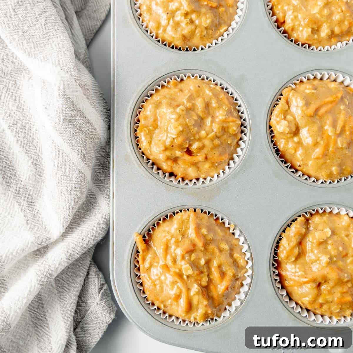 Moist Carrot Cake Muffins with Cream Cheese Swirl 7 Muffin tray filled with batter ready to bake. A patterned cloth is placed beside the tray on a white surface.