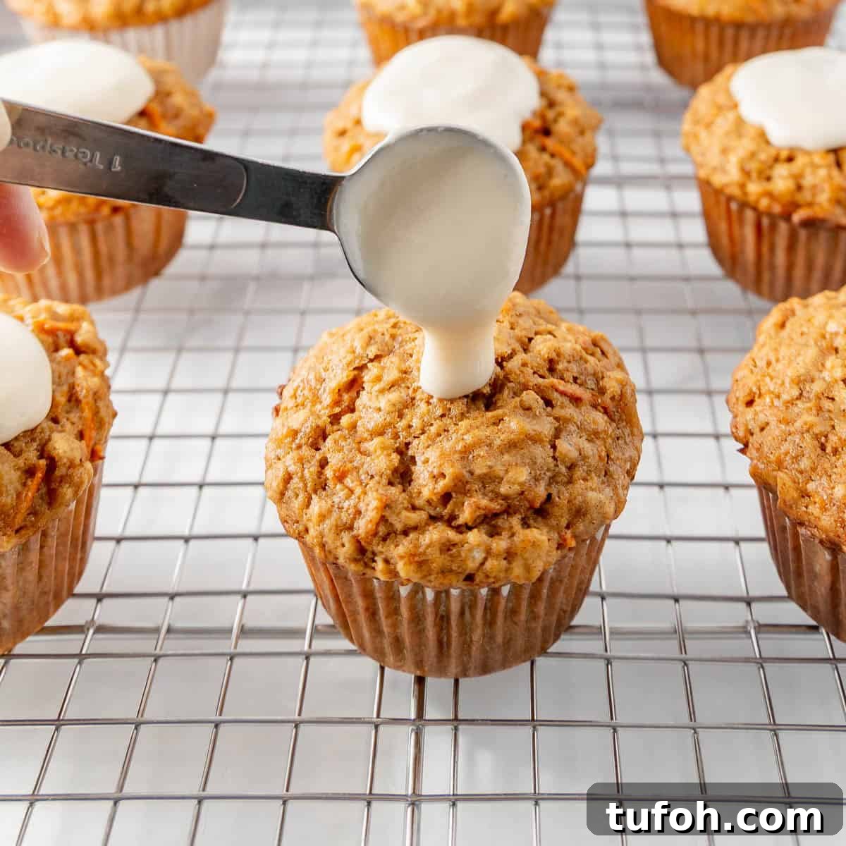 Moist Carrot Cake Muffins with Cream Cheese Swirl 9 Muffins on a cooling rack with icing being spooned onto one.