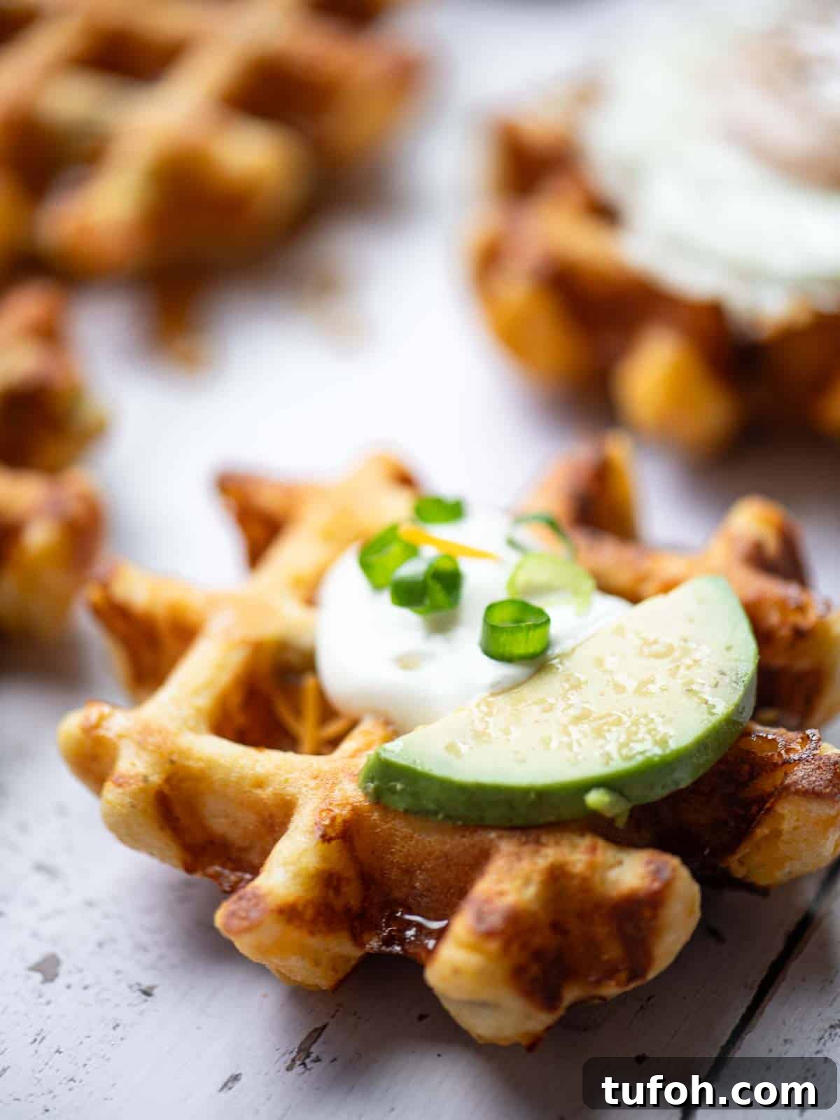 Spicy Green Chili Cheddar Waffles for Savory Brunch 6 Close up of a waffle with sour cream and sliced avocado on top.