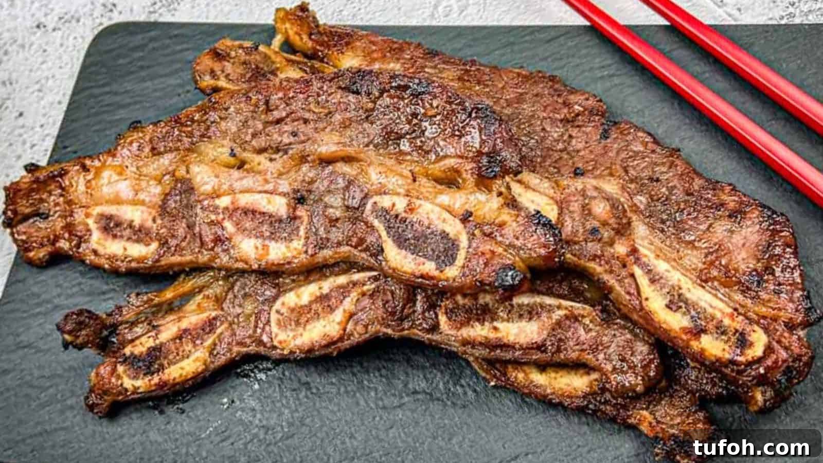 17 Crowd-Pleasing Backyard BBQ Recipes for Seconds-Worthy Meals 17 Korean Galbi Ribs on a slate platter with red chopsticks beside them.
