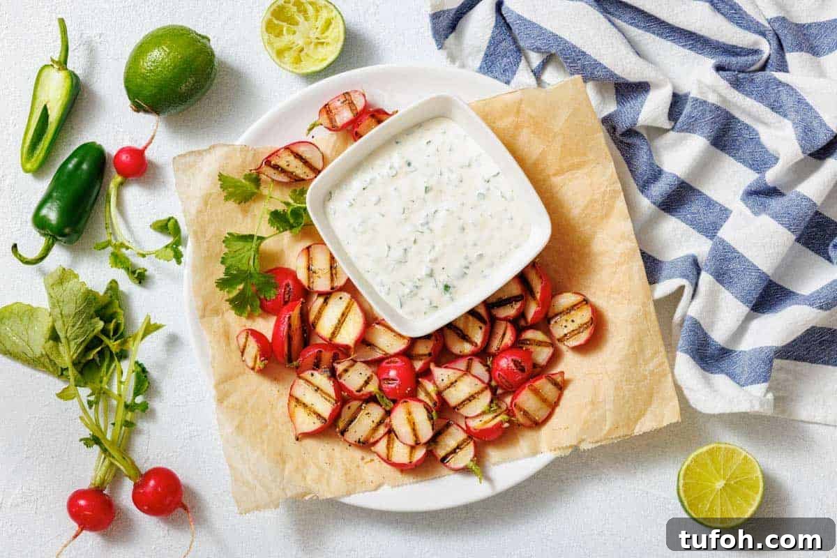 17 Crowd-Pleasing Backyard BBQ Recipes for Seconds-Worthy Meals 4 A plate with grilled radishes, a bowl of creamy dipping sauce, lime halves, jalapeño, and a striped cloth on a white surface.