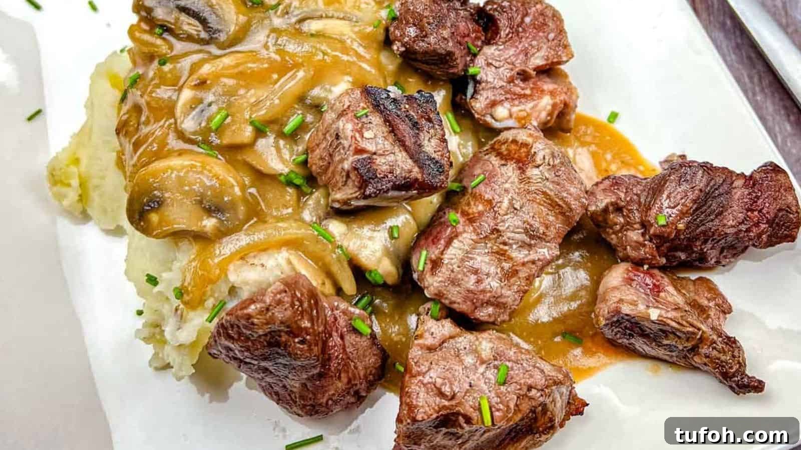 17 Crowd-Pleasing Backyard BBQ Recipes for Seconds-Worthy Meals 5 Texas Roadhouse Beef Tips with mushroom gravy over mashed potatoes, garnished with chives on a white plate.