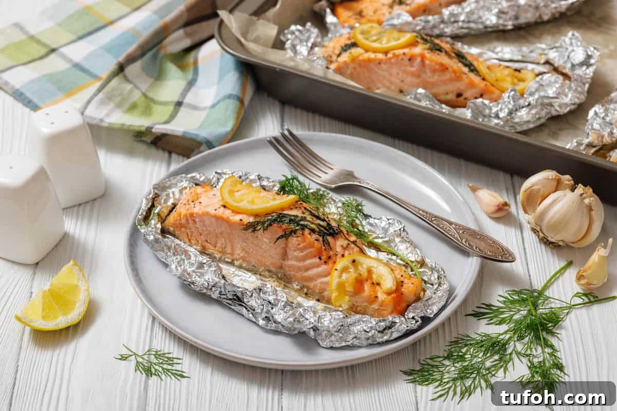 17 Crowd-Pleasing Backyard BBQ Recipes for Seconds-Worthy Meals 7 A close-up, slightly high-angle shot of a single Lemon Dill Salmon Foil Packets , seasoned with lemon and dill, still nestled in its aluminum foil packet on a light gray plate, with a silver fork to its right.
