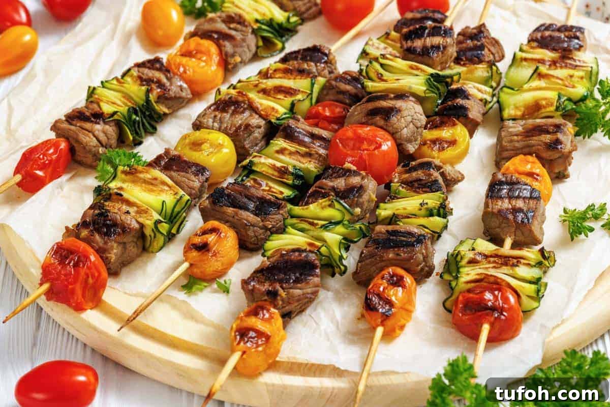 17 Crowd-Pleasing Backyard BBQ Recipes for Seconds-Worthy Meals 8 A wooden round serving board is covered with white parchment paper, displaying numerous grilled steak and veggie skewers arranged horizontally across it.