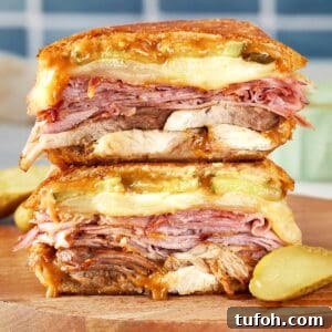 Stacked Cuban sandwich with layers of roast pork, ham, salami, Swiss cheese, pickles, and mustard, pressed until golden and melty.