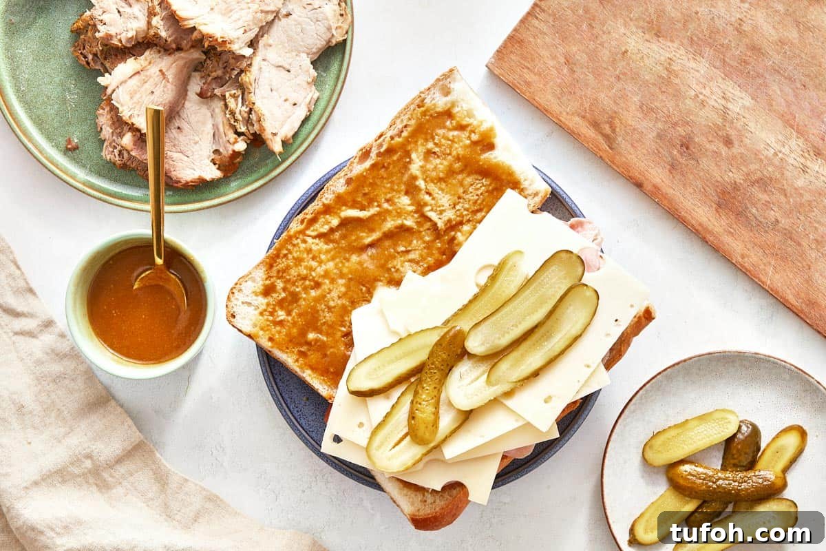 Cuban sandwich being assembled with pork, cheese, and pickles.