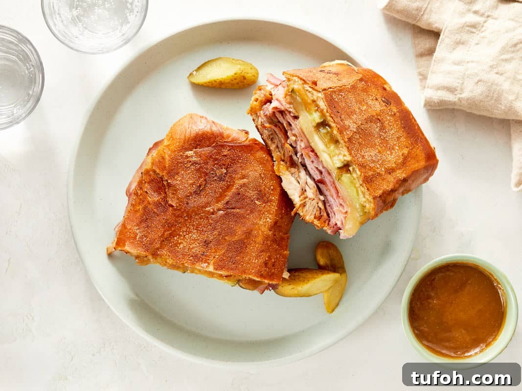 Cuban sandwich cut in half on a plate with pickles.