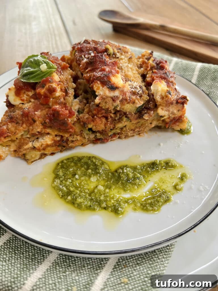 Zucchini Parmigiana with Ricotta: Layered Baked Zucchini Parmesan 19 Big piece of zucchini parmesan on plate with pesto garnish and wooden spoon in background.