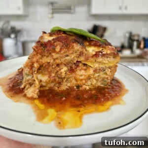 Zucchini Parmigiana with Ricotta: Layered Baked Zucchini Parmesan 21 Slice of zucchini parmigiana on white plate with stove and kitchen in background.