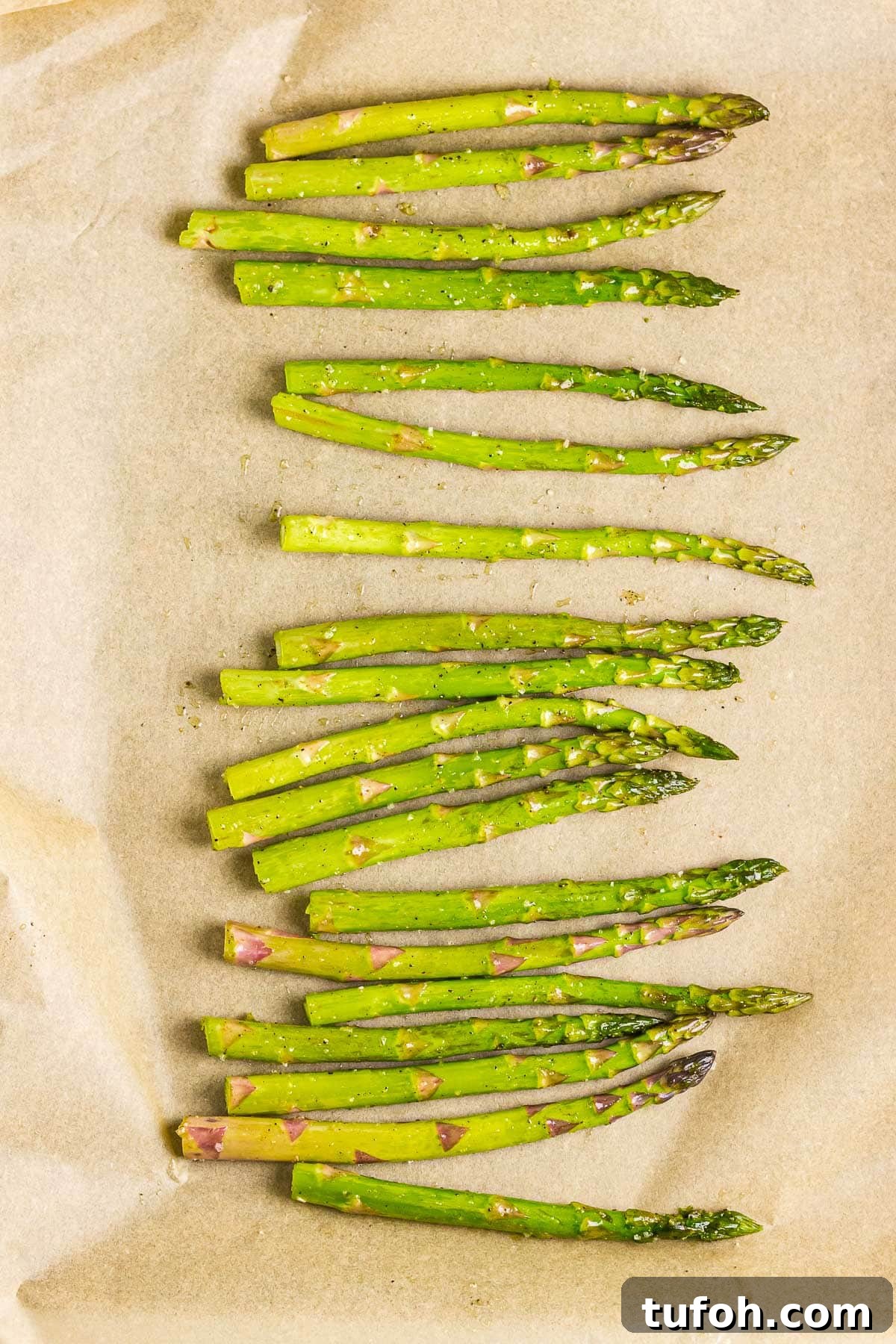 Crispy Oven-Roasted Asparagus with Garlic and Lemon 5 Seasoned asparagus spears on a parchment paper-lined baking sheet.